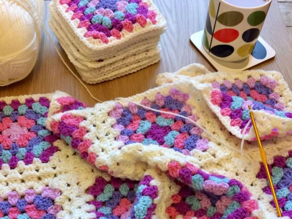 Photo of pink granny squares being joined with cream yarn on a table with a cup of tea and a ball of yarn