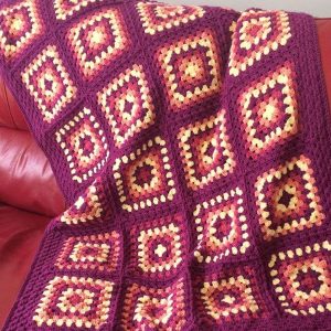 Granny Square Blanket in a range of red colours displayed on a red sofa