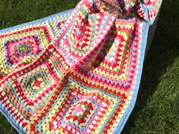 Cath Kidston inspired giant granny square blanket completed and draped in a basket on a lawn