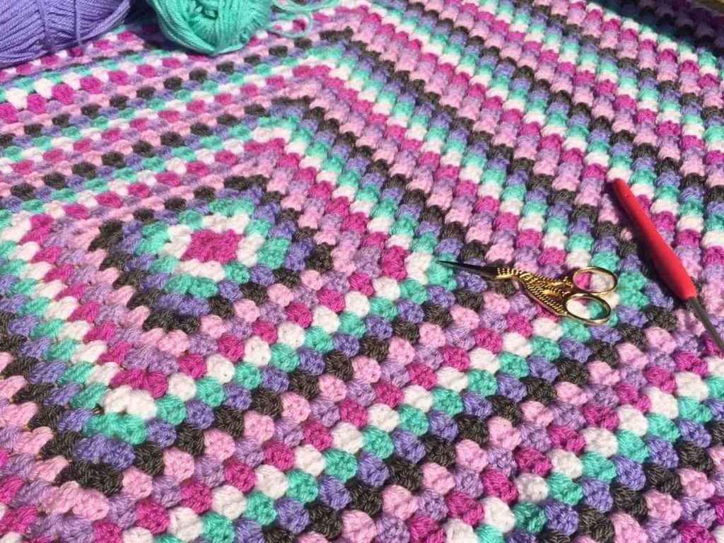 Close up of a giant Granny Square made with pinks and purple colours
