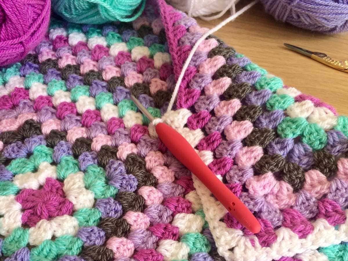 Red crochet hook working rounds of a granny square