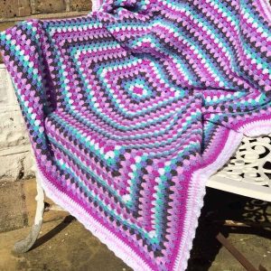 Finished Amethyst Granny Square Blanket displayed on a garden bench