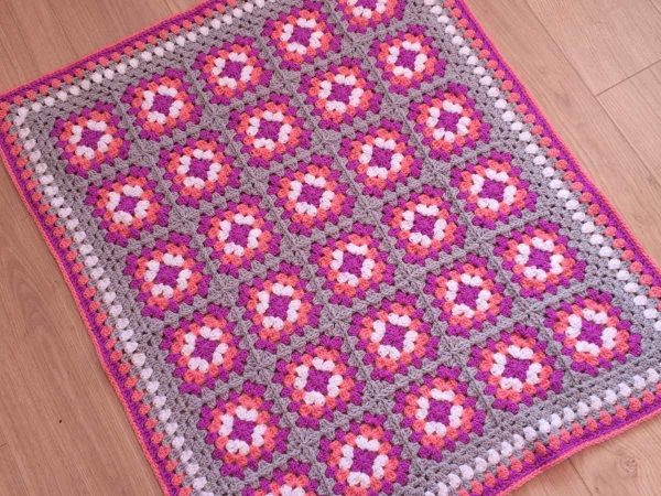 Granny Square blanket made in pink laid on a wood floor