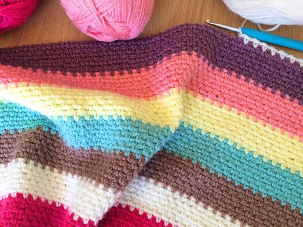 Neapolitan Blanket - a corner to corner moss stitch blanket being worked in stripes with a blue crochet hook