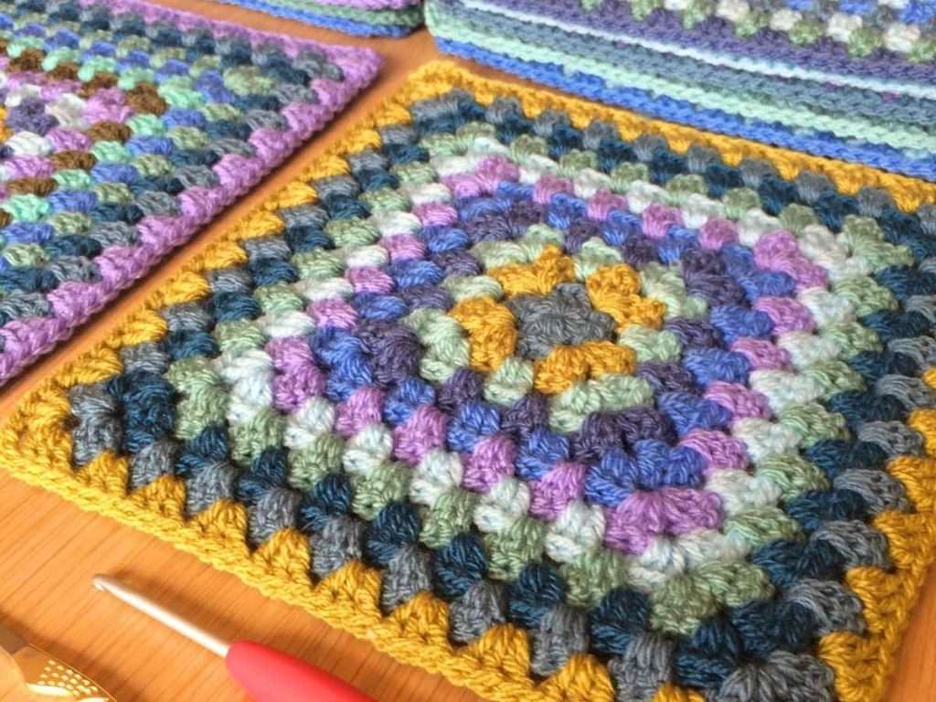 Close up of large Granny Squares on a table with a red crochet hook