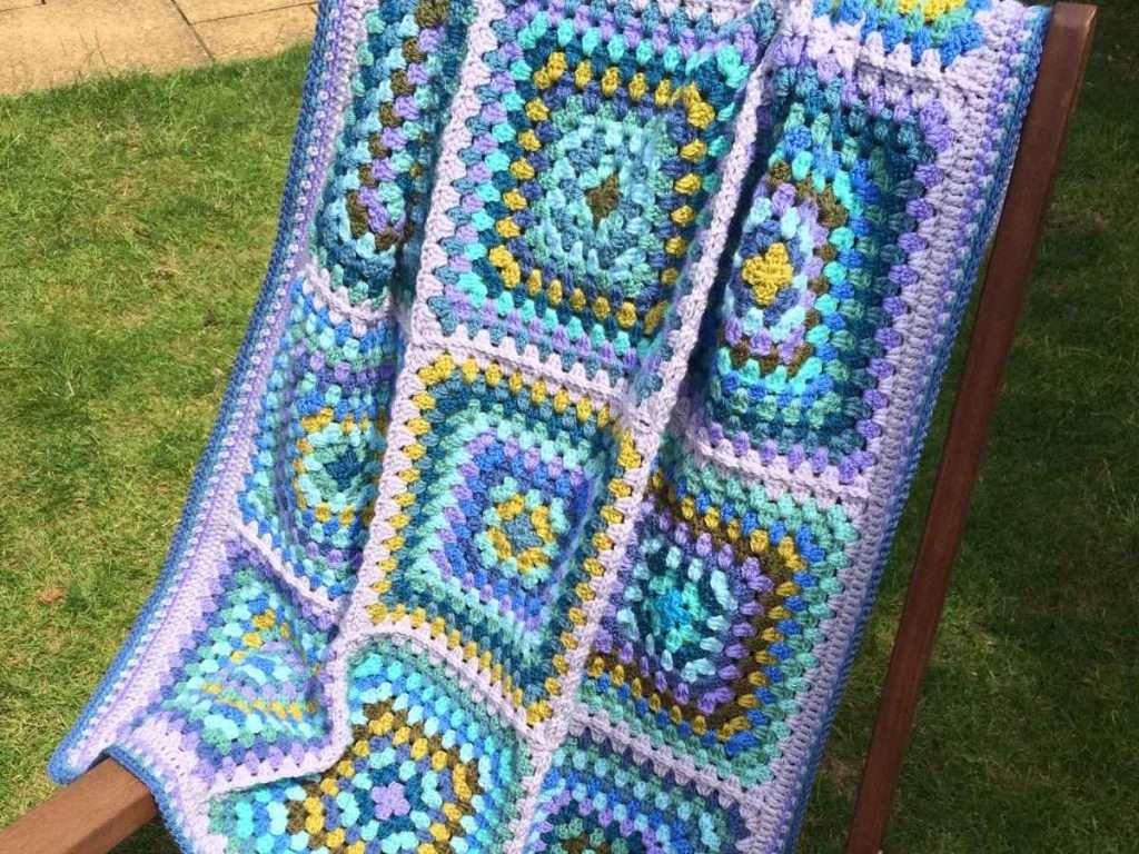 Finished Mellow Granny Square Blanket arranged on a wooden chain in a garden