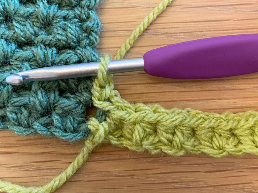 Light green crochet stitches joining a dark green section with a purple crochet hook