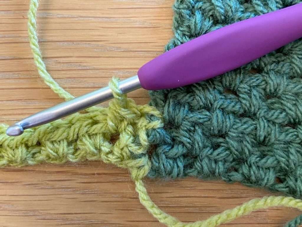 Crochet stitches in green yarn with a purple crochet hook