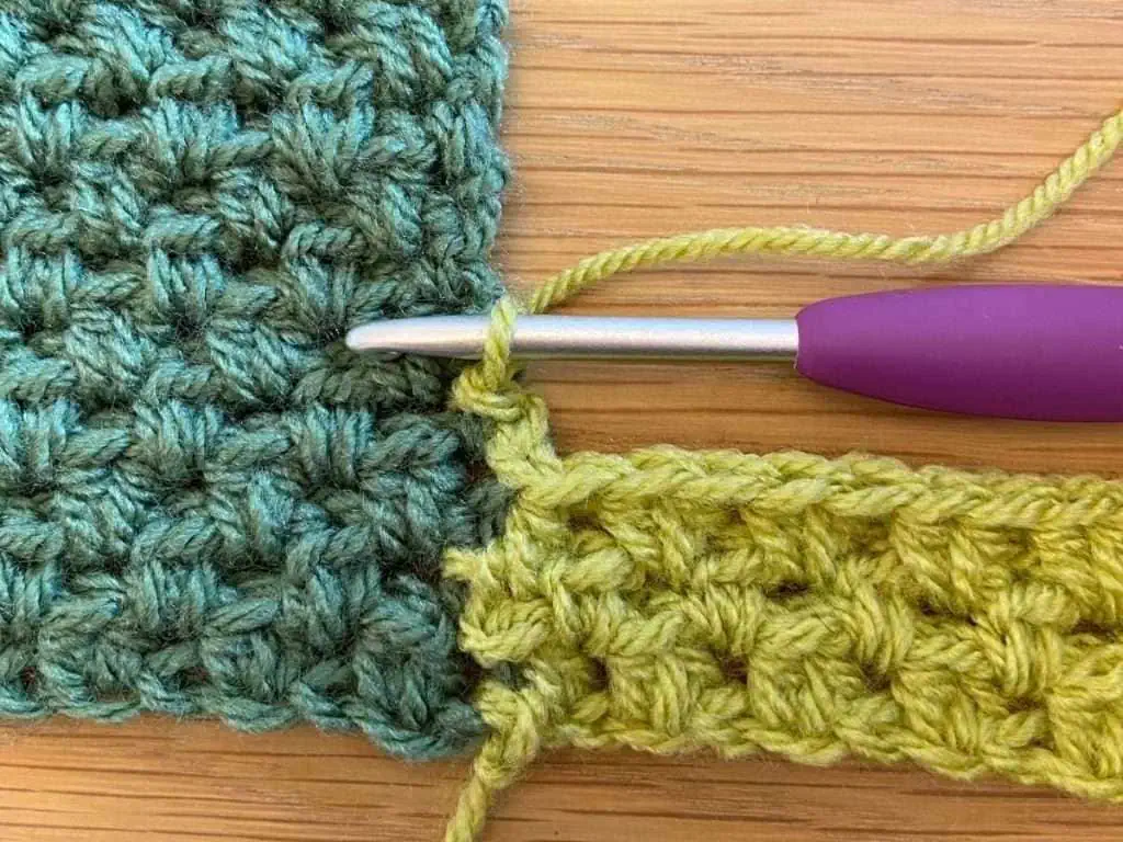 Close up of crochet stitches made with light and dark green yarn and a hook