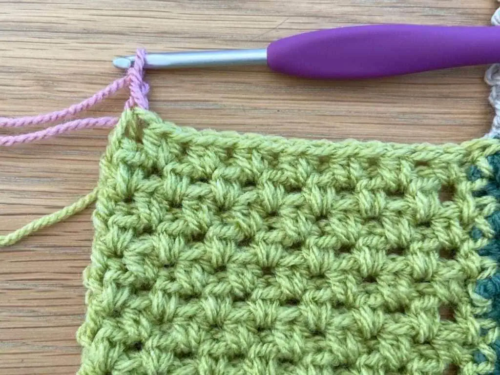 Pink yarn being added to green piece of crochet
