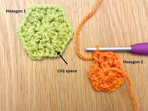 Completed green crochet hexagon next to a partly made orange hexagon ready to join the two