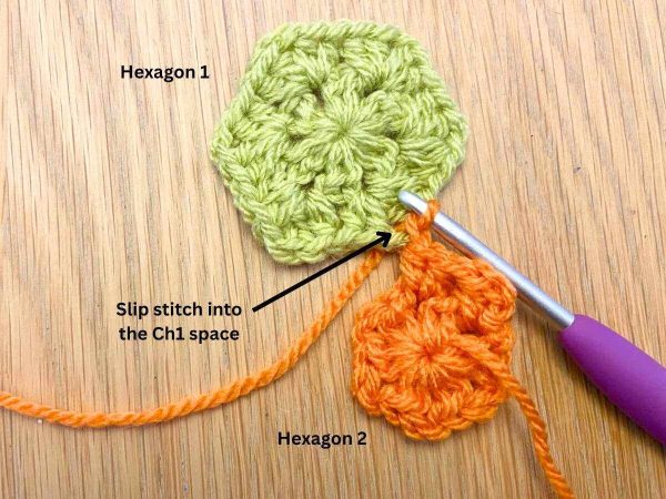 Orange crochet hexagon being joined to a completed green hexagon with a purple crochet hook