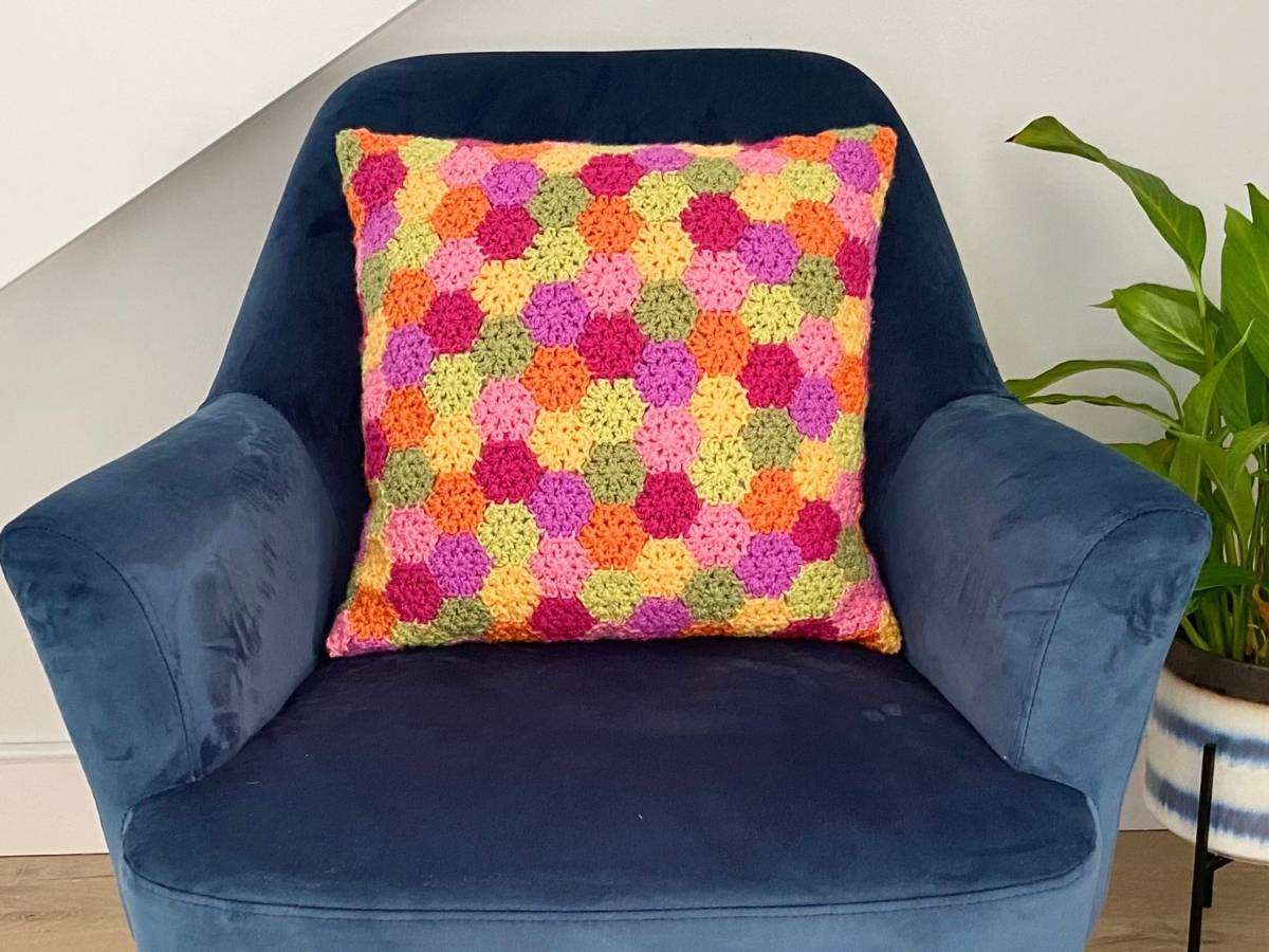Brightly coloured crochet hexagon cushion on a blue armchair