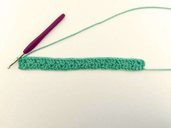 Row two of the heart block blanket using green yarn and a crochet hook