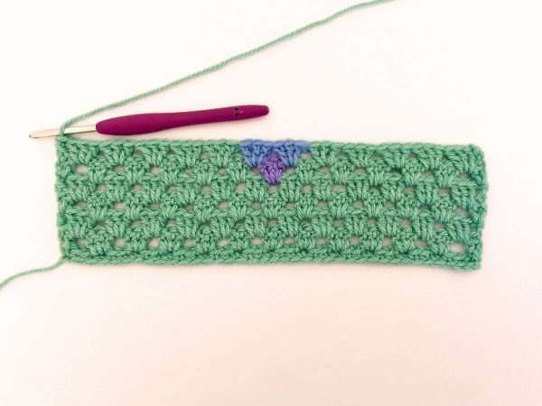 Green yarn and purple crochet hook used to indicate row 7 of the crochet pattern and showing the colour changes of the row to create a heart