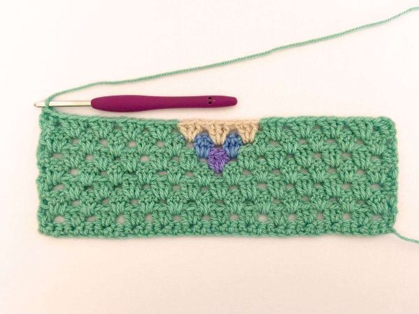 Green yarn and purple crochet hook used to indicate row 8 of the crochet pattern and showing the colour changes of the row to create a heart