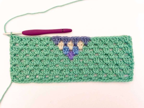 Green yarn and purple crochet hook used to indicate row 9 of the crochet pattern and showing the colour changes of the row to create a heart