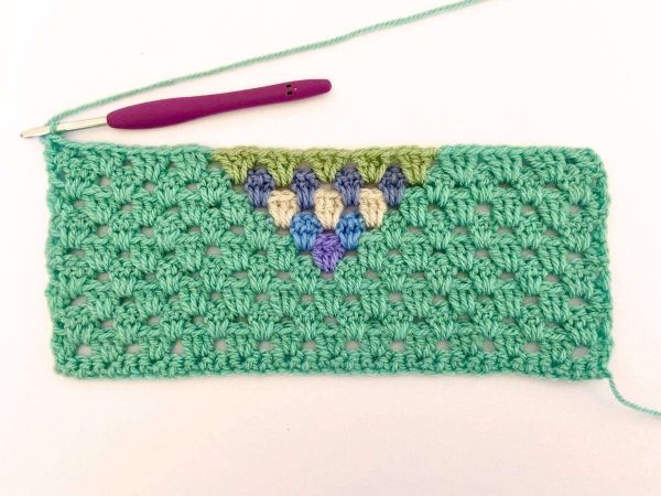 Green yarn and purple crochet hook used to indicate row 10 of the crochet pattern and showing the colour changes of the row to create a heart