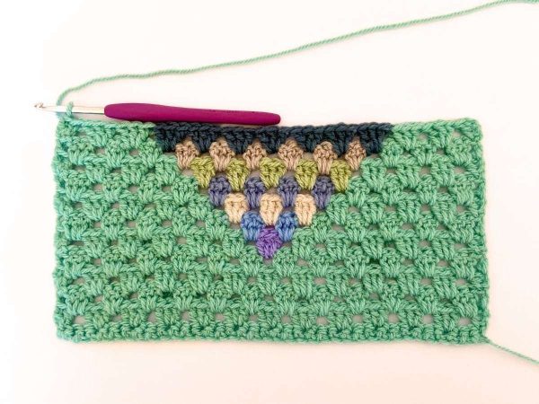 Green yarn and purple crochet hook used to indicate row 12 of the crochet pattern and showing the colour changes of the row to create a heart