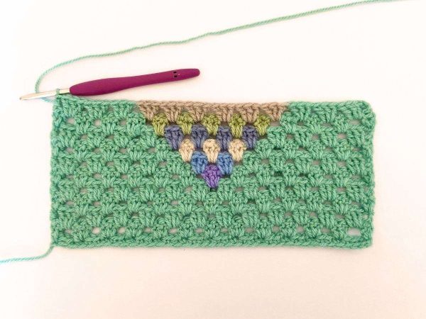 Green yarn and purple crochet hook used to indicate row 11 of the crochet pattern and showing the colour changes of the row to create a heart