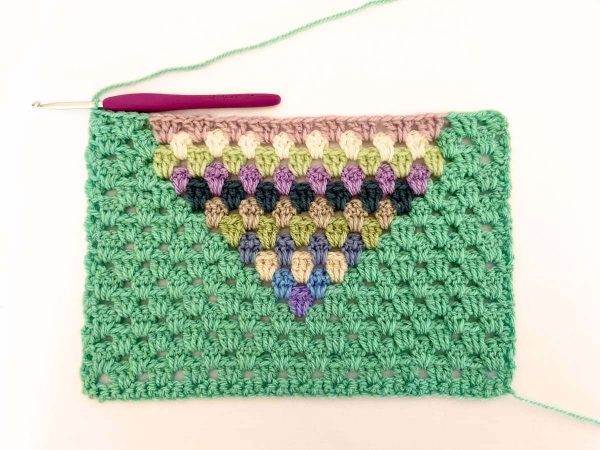 Green yarn and purple crochet hook used to indicate row 16 of the crochet pattern and showing the colour changes of the row to create a heart