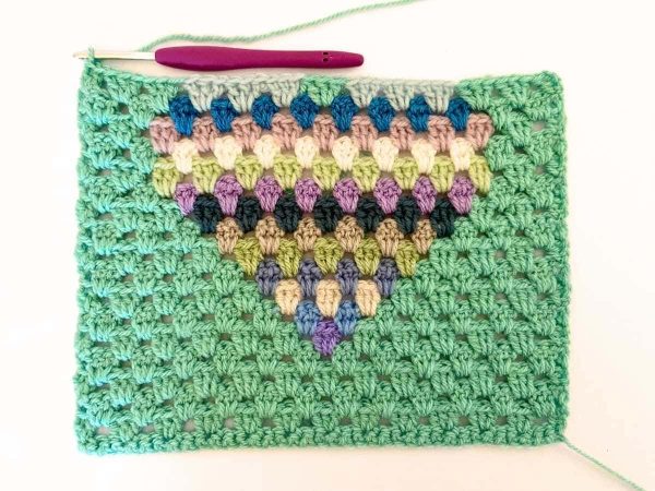 Green yarn and purple crochet hook used to indicate row 18 of the crochet pattern and showing the colour changes of the row to create a heart