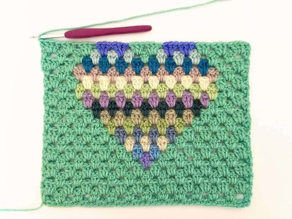 Green yarn and purple crochet hook used to indicate row 19 of the crochet pattern and showing the colour changes of the row to create a heart