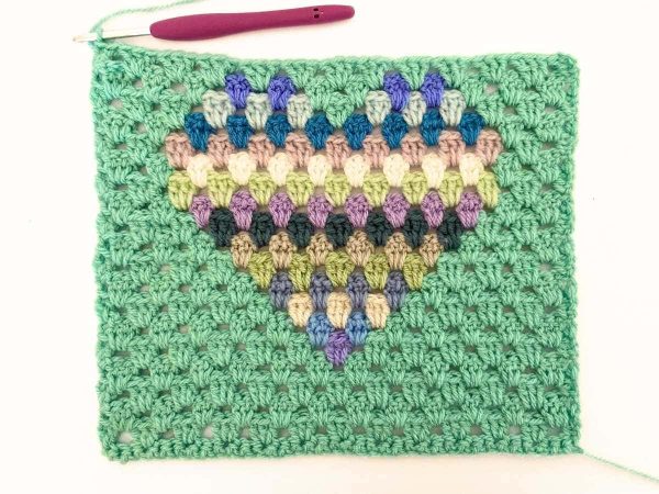 Green yarn and purple crochet hook used to indicate row 20 of the crochet pattern and showing the colour changes of the row to create a heart