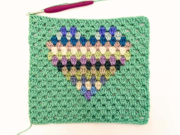 Green yarn and purple crochet hook used to indicate row 21 of the crochet pattern and showing the colour changes of the row to create a heart