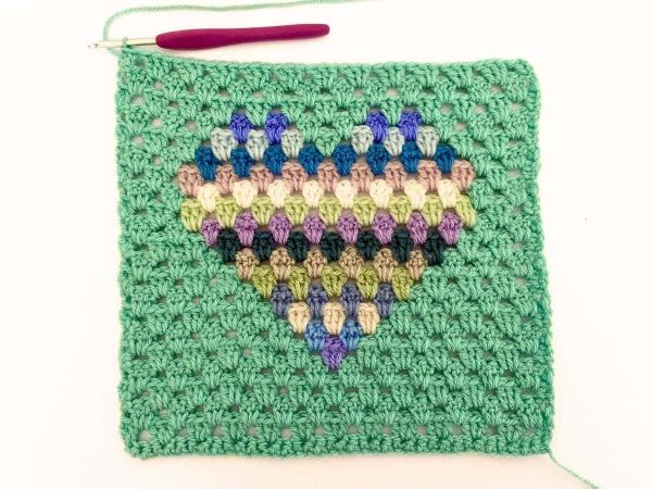 Green yarn and purple crochet hook used to indicate row 22 of the crochet pattern and showing the colour changes of the row to create a heart