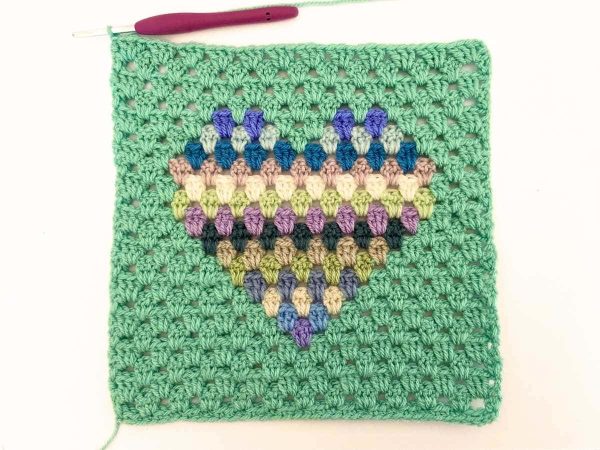 Green yarn and purple crochet hook used to indicate row 23 of the crochet pattern and showing the colour changes of the row to create a heart