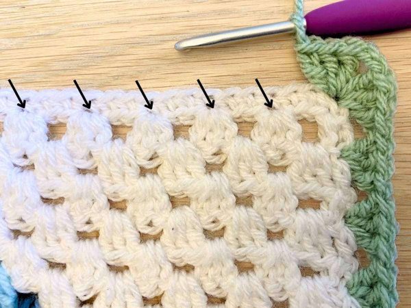 Working the border along the bottom of a crochet blanket with arrows indicating stitch placement
