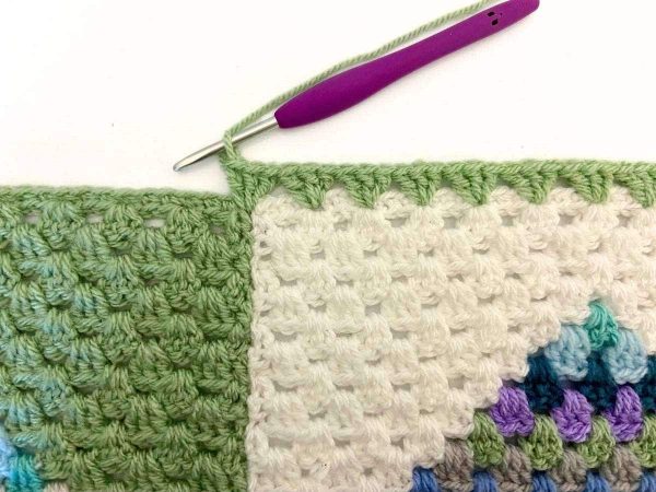 Working the border across the bottom of the Heart Block Blanket indicating the placement of stitches as you work across the join of two blocks