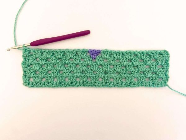 Green yarn and purple crochet hook used to indicate row 6 of the crochet pattern and showing the colour changes of the row to create a heart