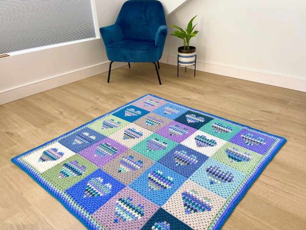 Completed crochet Heart Block Blanket laid out on a wooden floor next to a chair and an indoor plant