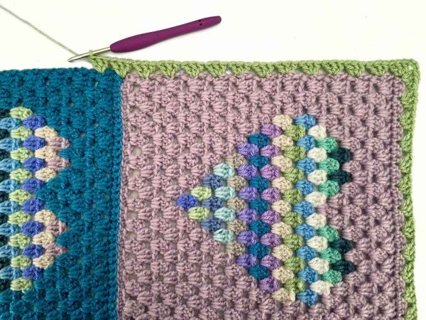 Green crochet border being worked around the Heart Block Blanket